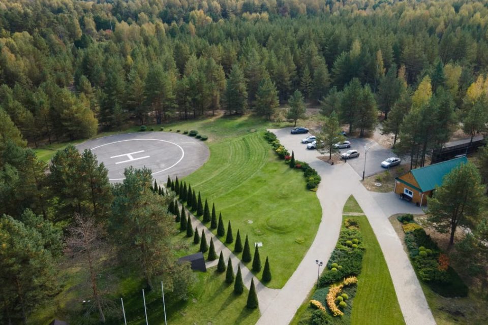 Aerial shot of a forest with a helipad, parking area, and landscaped gardens.